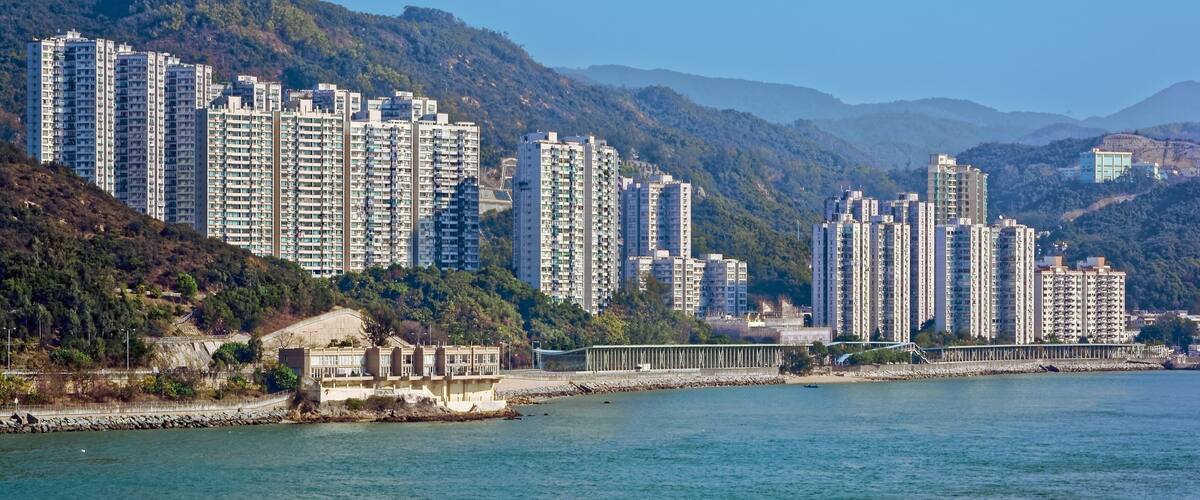 A coastal cityscape with high-rise residential buildings, a bridge, and a mountainous backdrop.