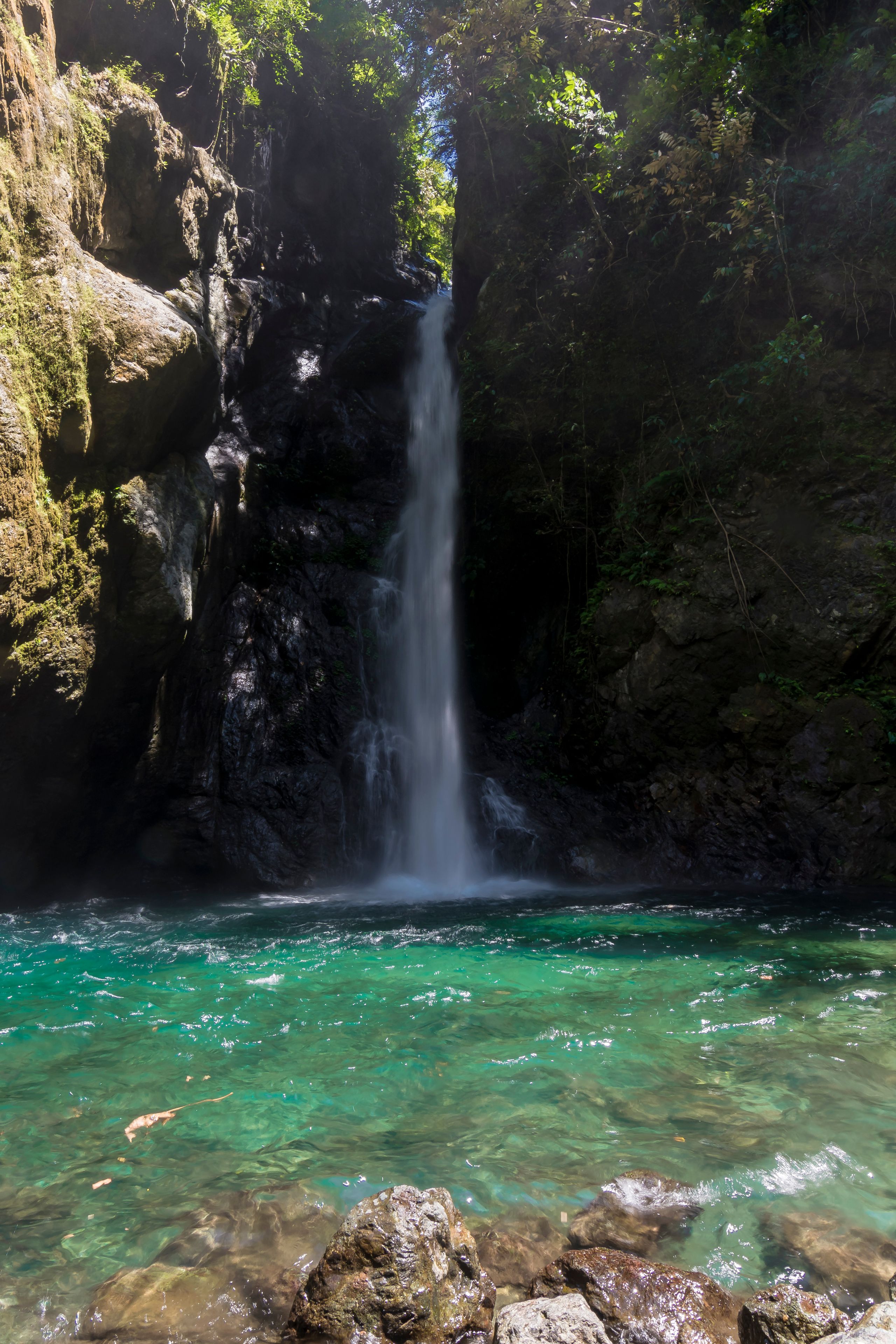 A waterfall cascading into a clear turquoise pool surrounded by rocky cliffs and lush greenery.