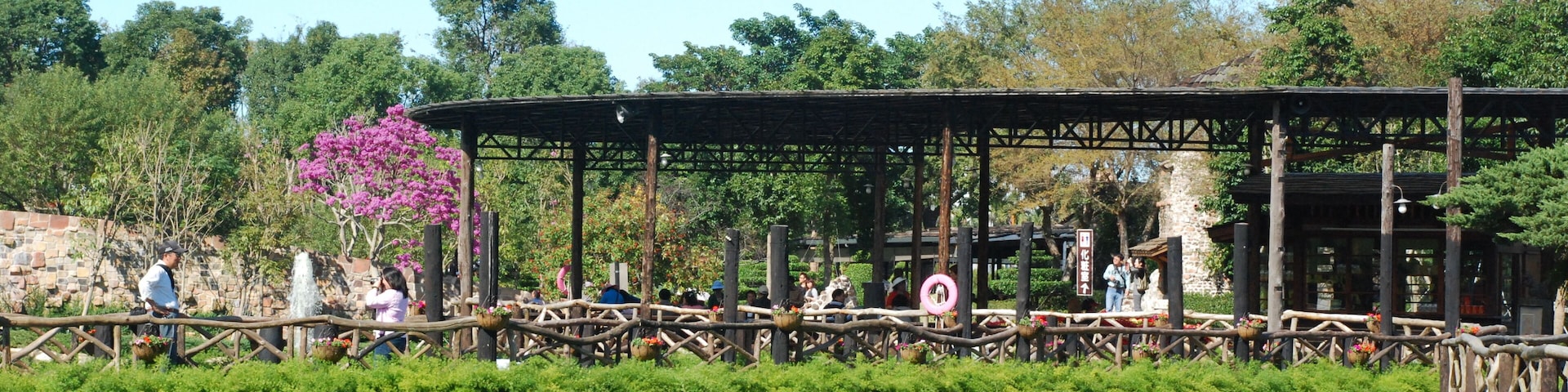 Un pont en bois enjambant une étendue d’eau, avec de la végétation, un mur de pierre et des arbres en arrière-plan.
