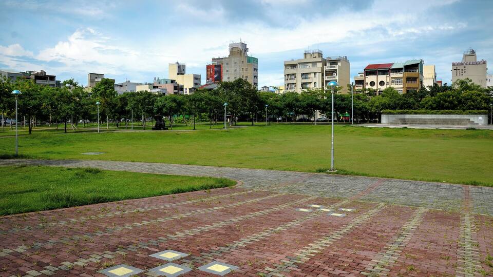 A park with a paved walkway, green grass, and trees.