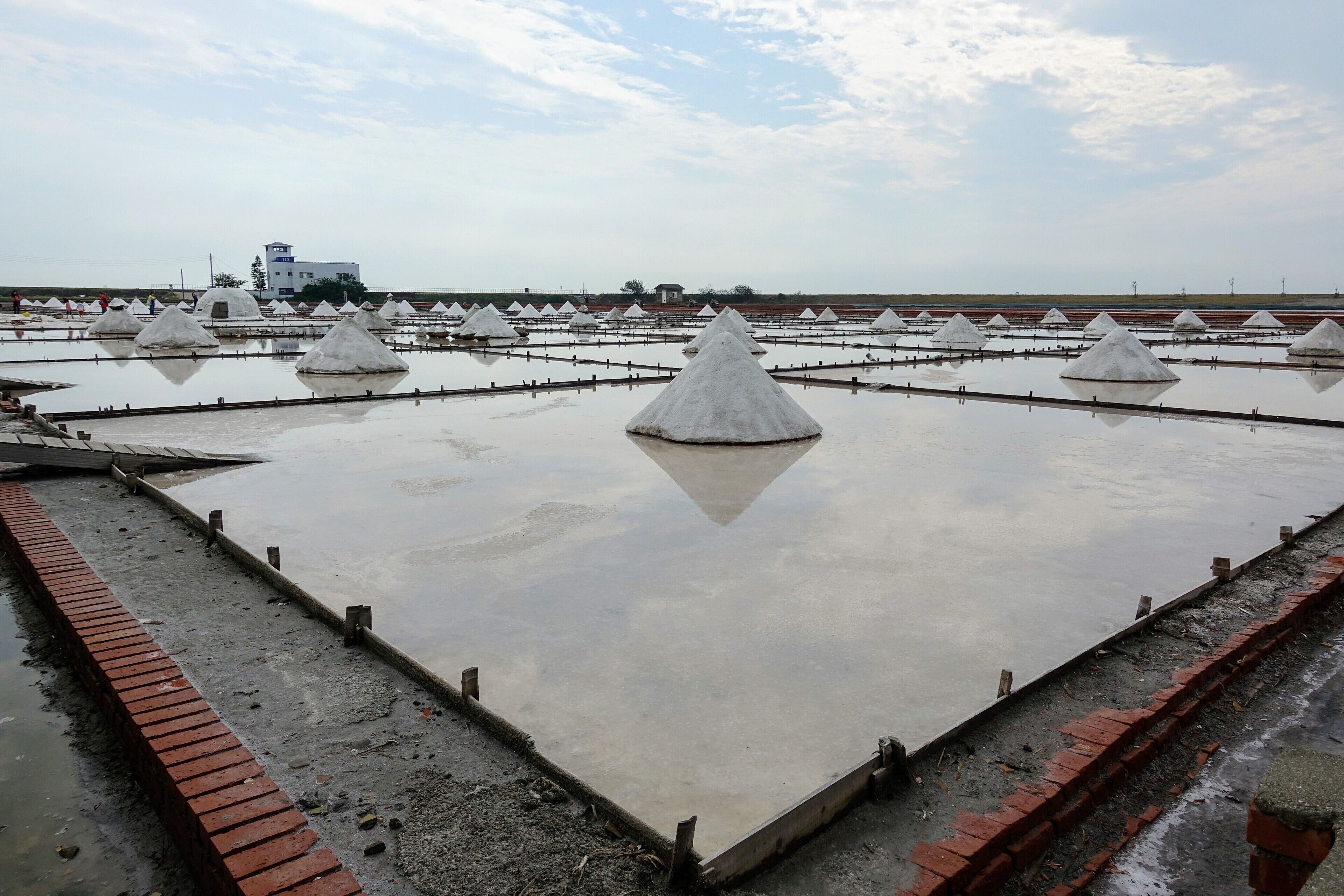 A salt flat with white conical structures and a distant building.