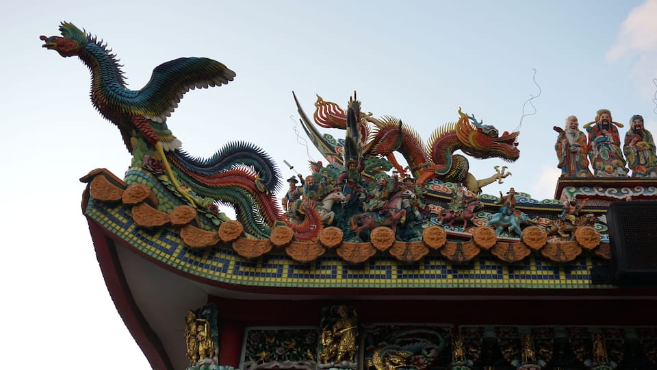 A colorful dragon sculpture atop a traditional building with intricate roof tiles and golden decorations.