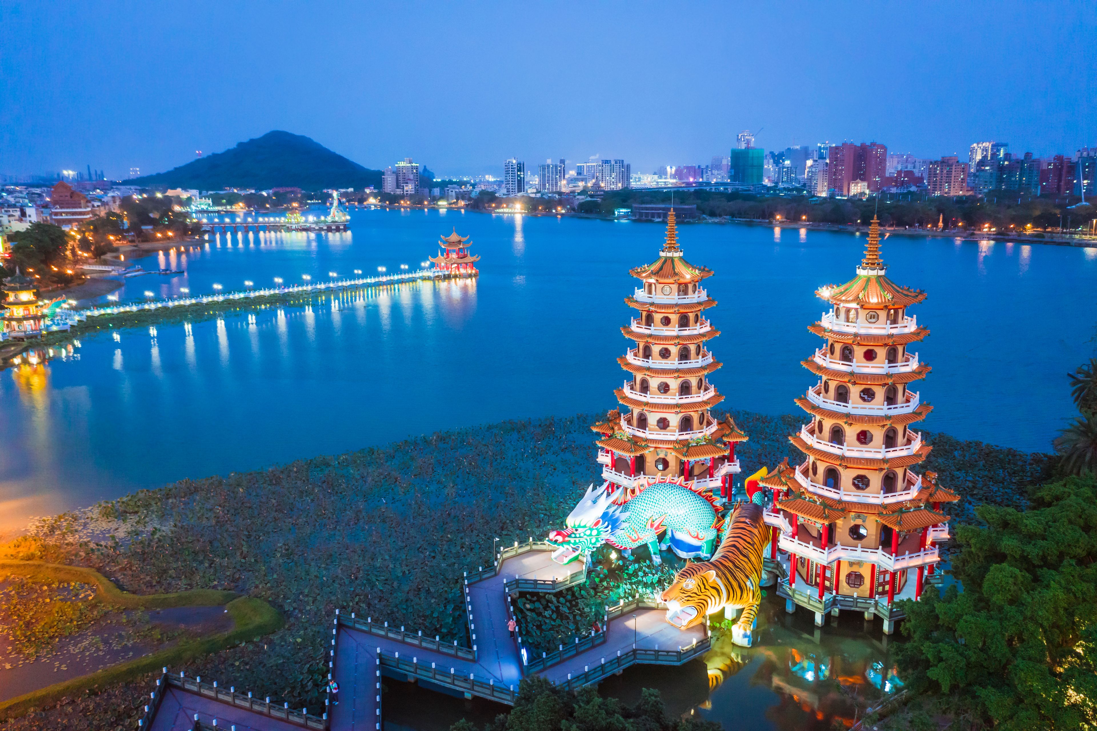 A night view of a cityscape with two illuminated pagodas by a calm river.