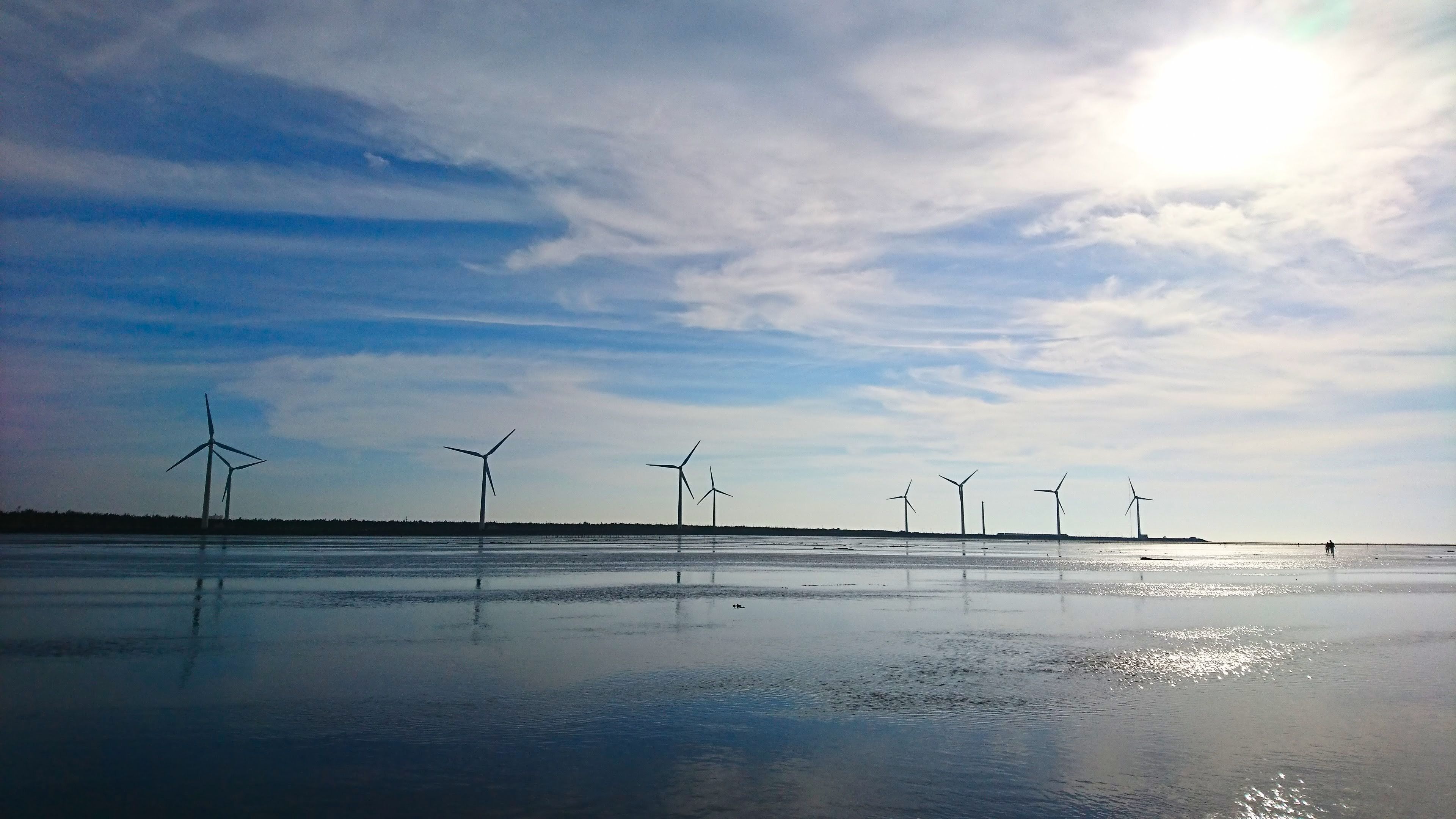 Un cuerpo de agua tranquila con aerogeneradores al fondo.