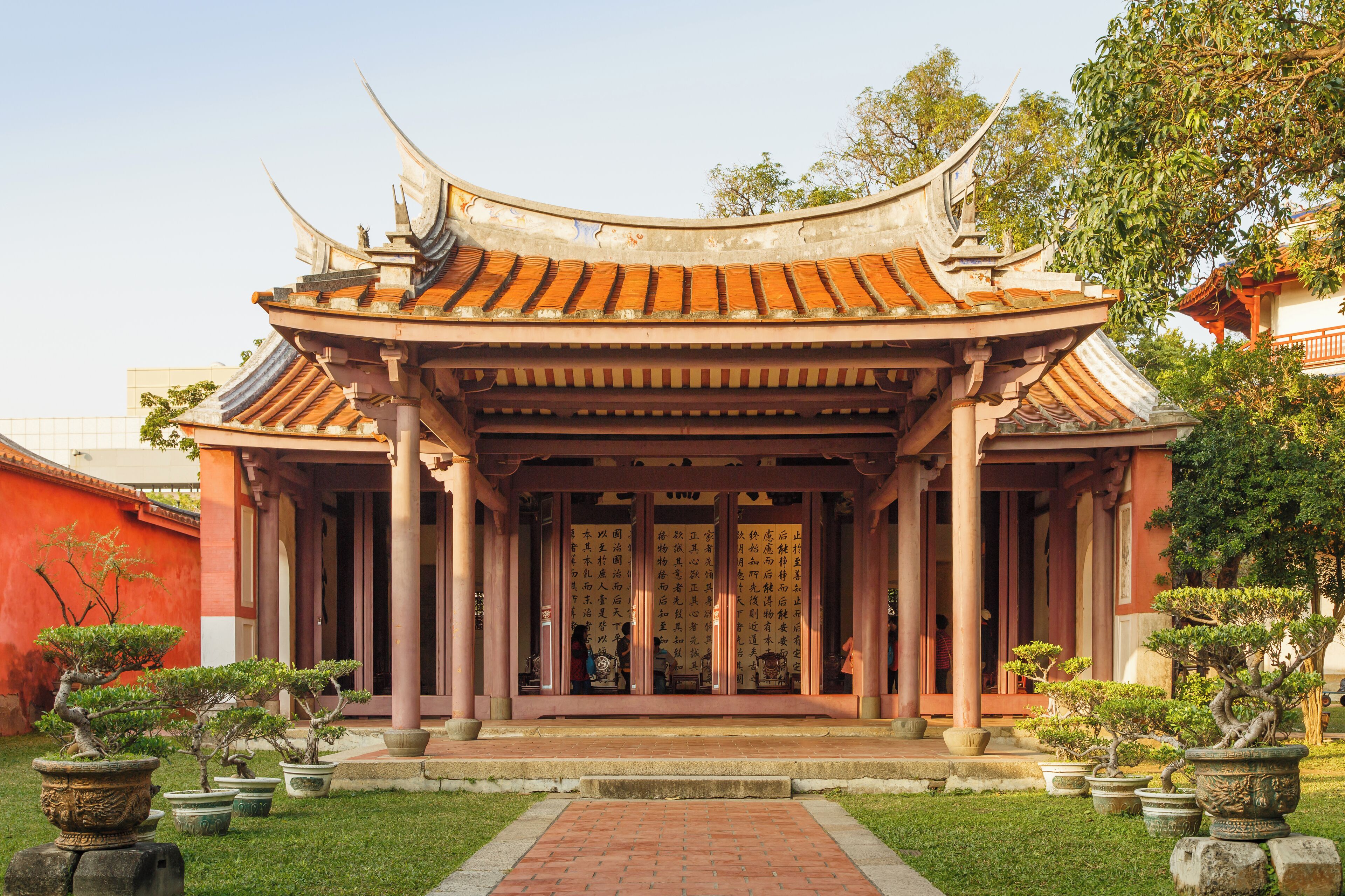 A traditional temple with a curved roof, columns, and a garden with potted plants.