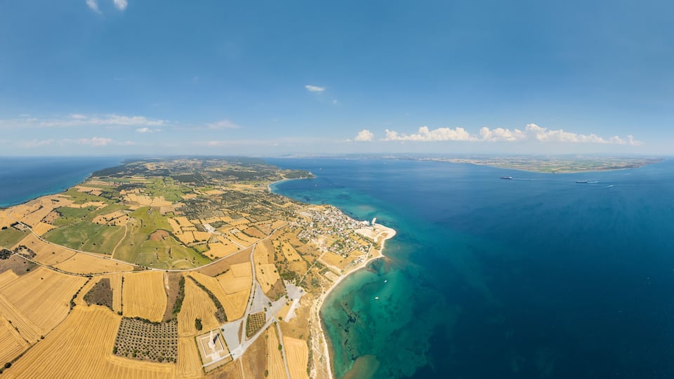 An aerial view of a coastal landscape with fields, a beach, and a distant island.