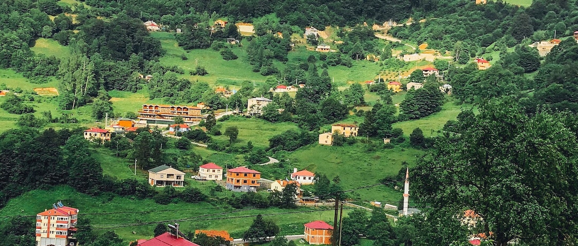Un paisaje rural con colinas onduladas, casas dispersas y un campanario de iglesia destacado.