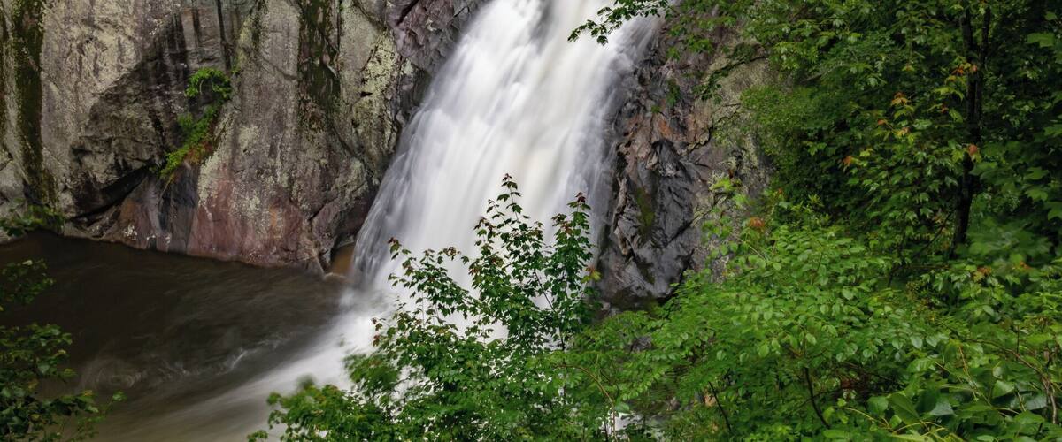 A waterfall cascading down a rocky cliff surrounded by lush greenery.