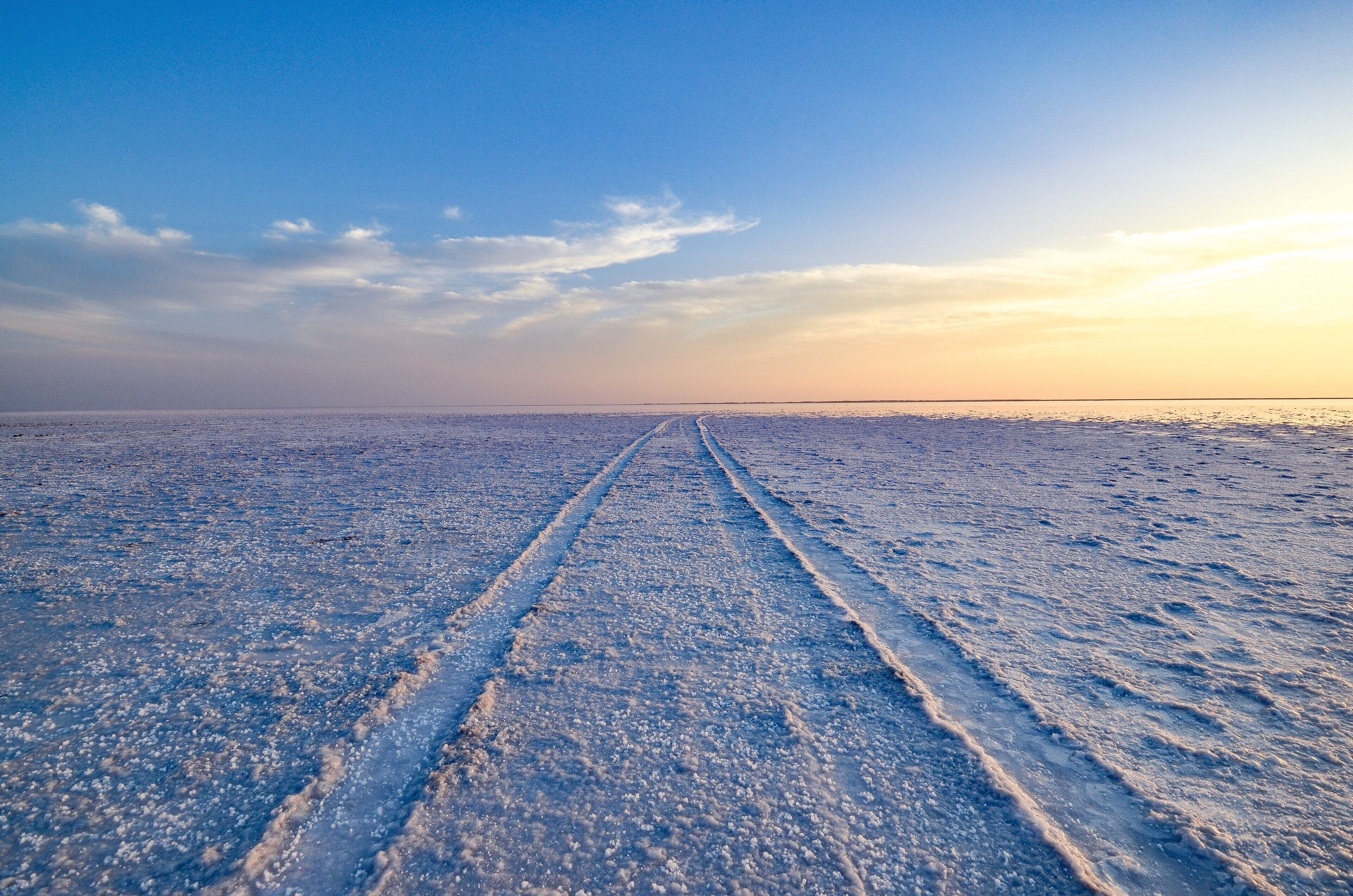 A frozen landscape with tire tracks leading towards the horizon.