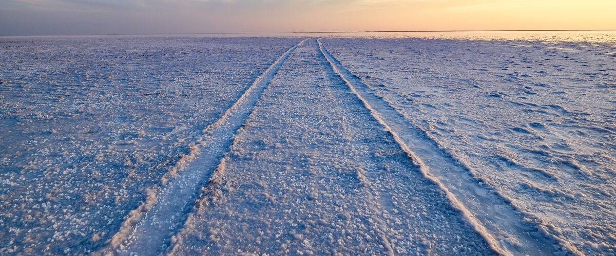 A frozen landscape with tire tracks leading towards the horizon.