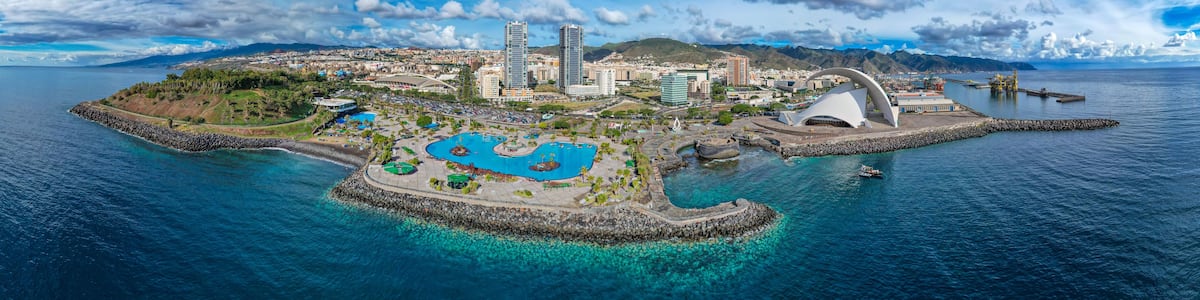 A coastal cityscape with a prominent white building, a marina, and clear blue waters.