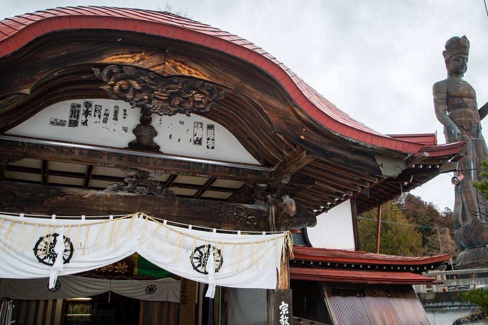 Un edificio japonés tradicional con tejado rojo y una estatua grande al fondo.