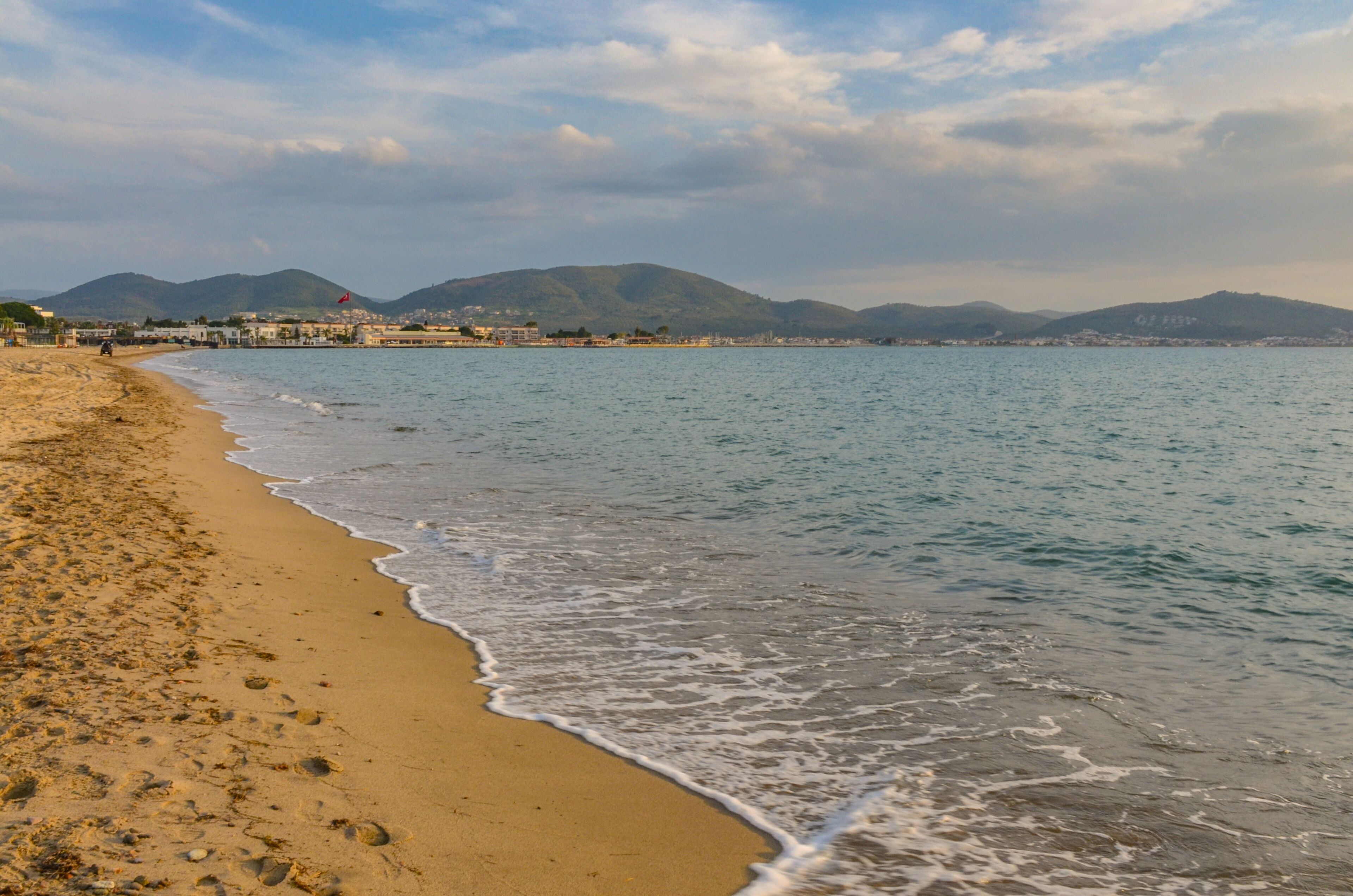 A beach with gentle waves, a clear sky, and distant mountains.