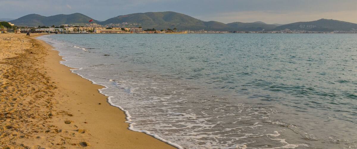 A beach with gentle waves, a clear sky, and distant mountains.