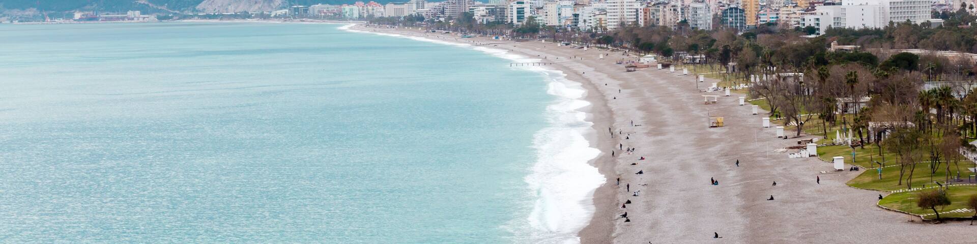 A coastal city with a beach, buildings, and mountains in the background.