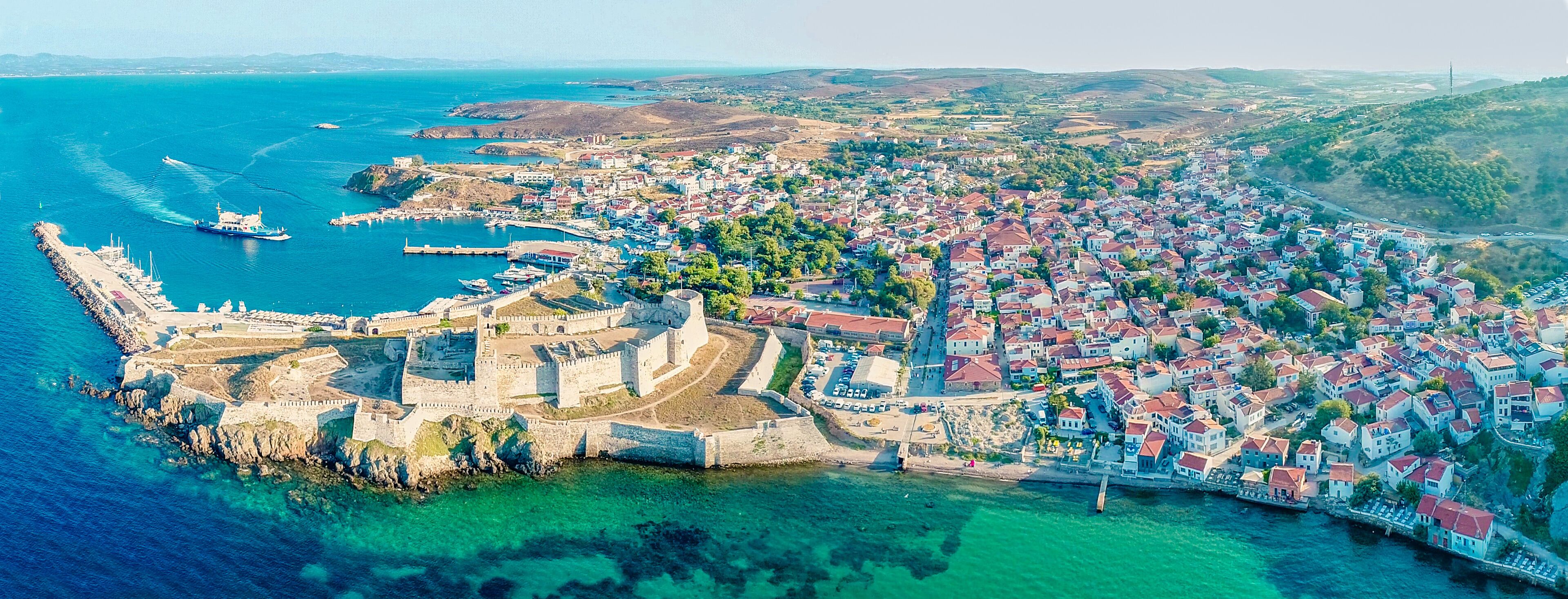 An aerial view of a coastal town with a historic fortification, a harbor with boats, and a densely built residential area.