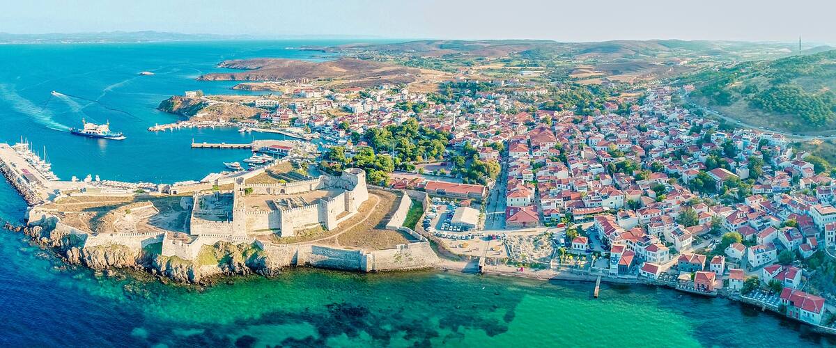 An aerial view of a coastal town with a historic fortification, a harbor with boats, and a densely built residential area.