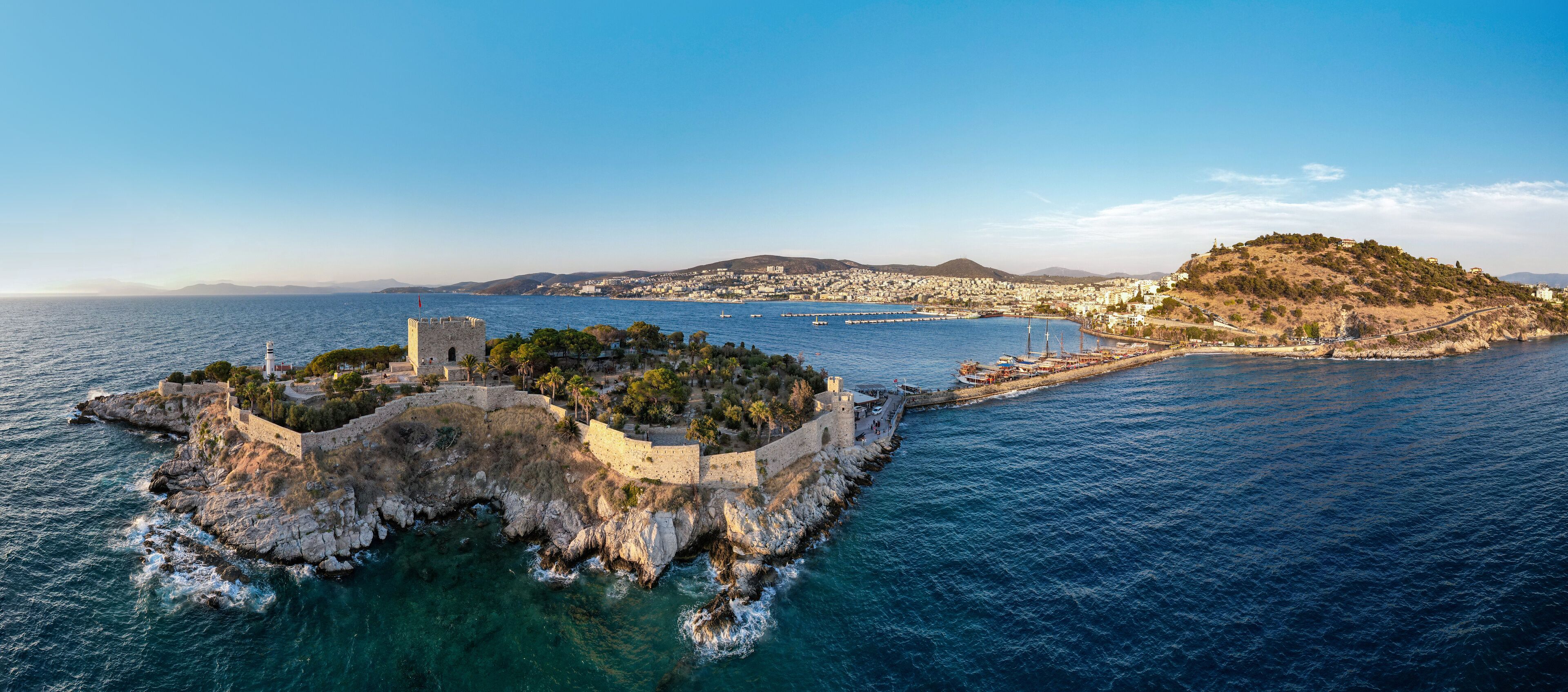 A coastal city with a historic fortress, a harbor with boats, and a hilltop with buildings.