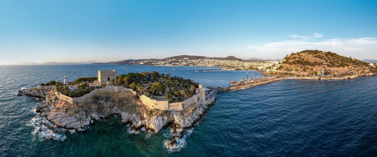 A coastal city with a historic fortress, a harbor with boats, and a hilltop with buildings.
