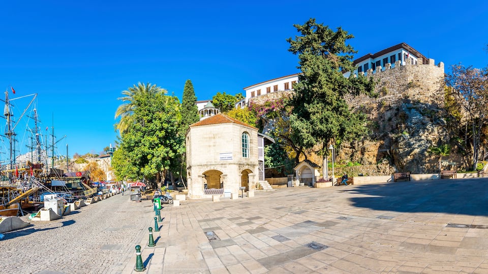 A historic square with a prominent building, a waterfront with boats, and lush trees.