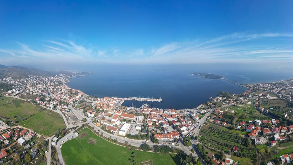 An aerial view of a coastal town with a marina, green fields, and a large body of water.