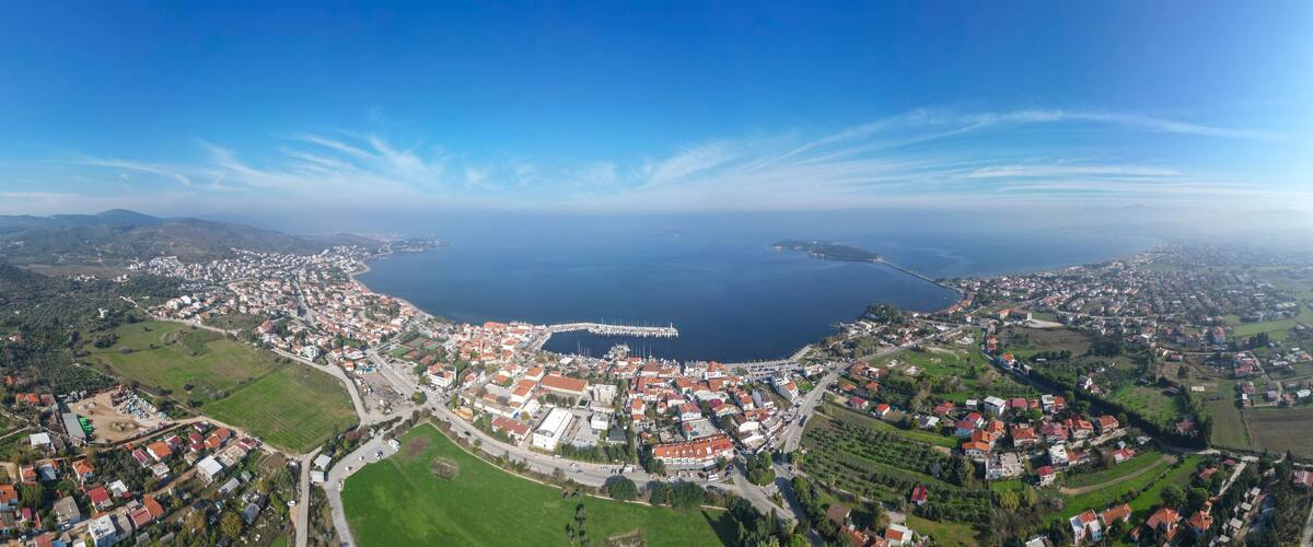 An aerial view of a coastal town with a marina, green fields, and a large body of water.