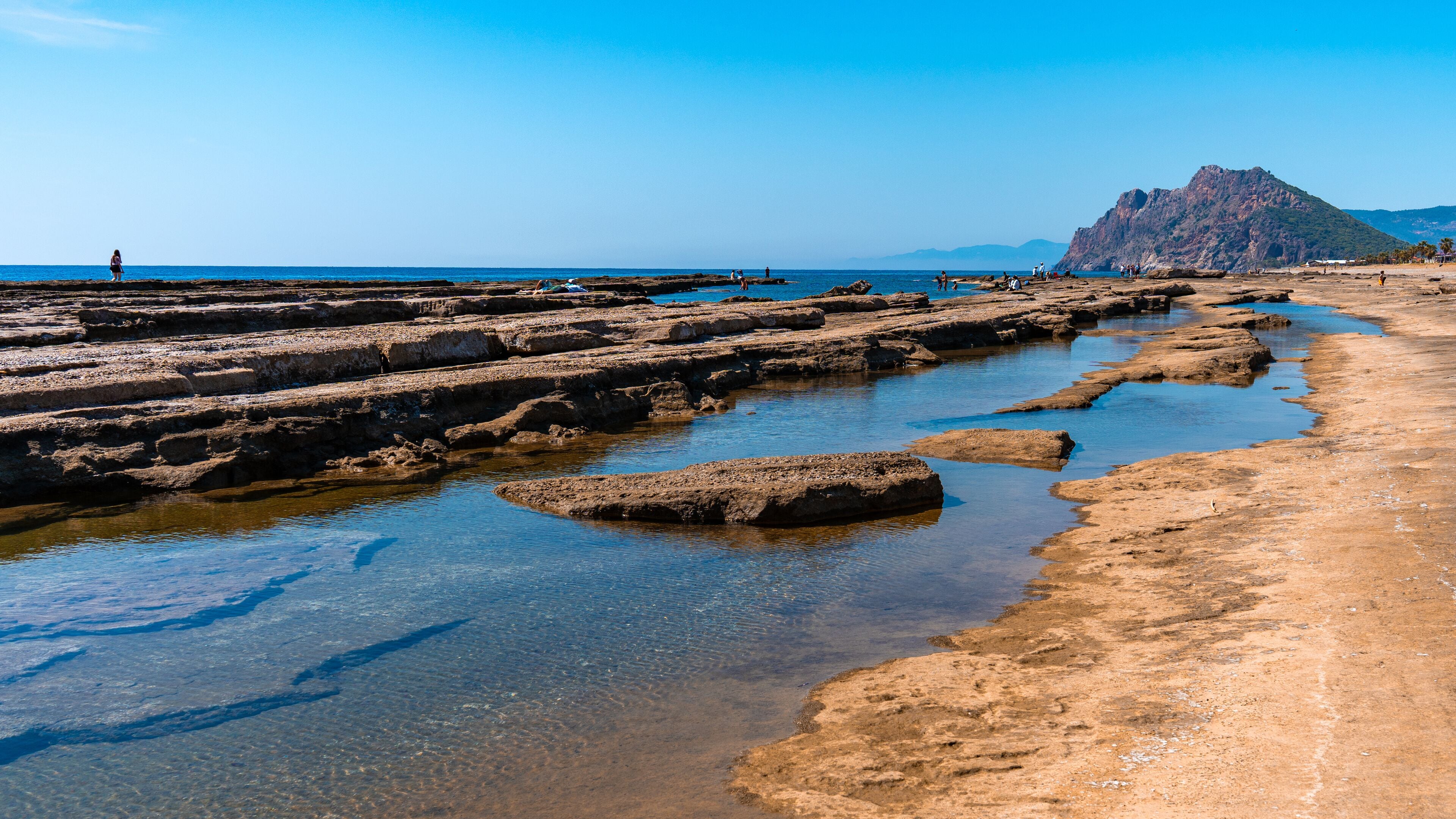A rocky beach with clear water and a mountain in the background.