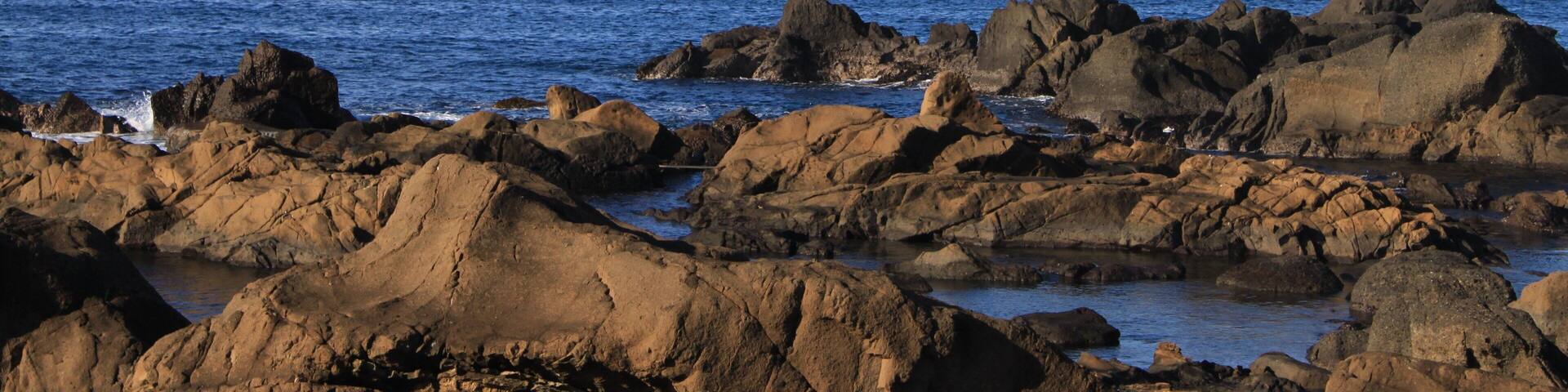 A rocky coastline with waves crashing against the rocks under a clear sky.