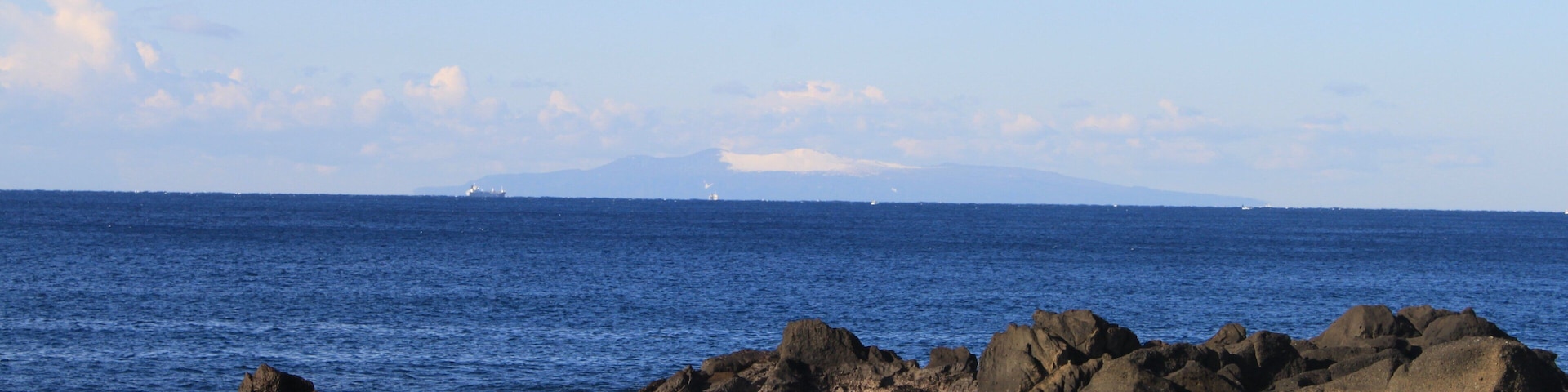 Una costa rocosa con olas rompiendo contra las rocas bajo un cielo despejado.