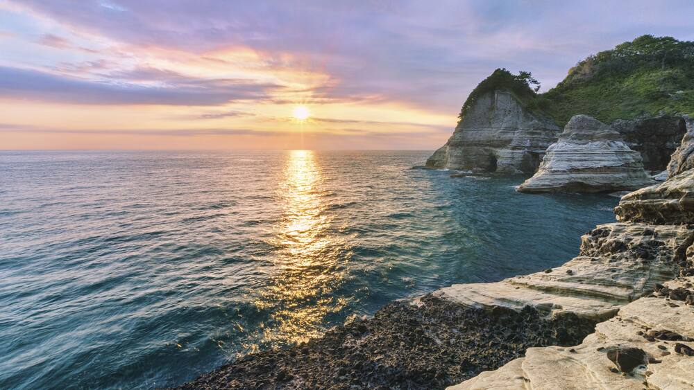Un coucher de soleil sur la côte, avec un ciel dégagé, des falaises rocheuses et une mer calme.