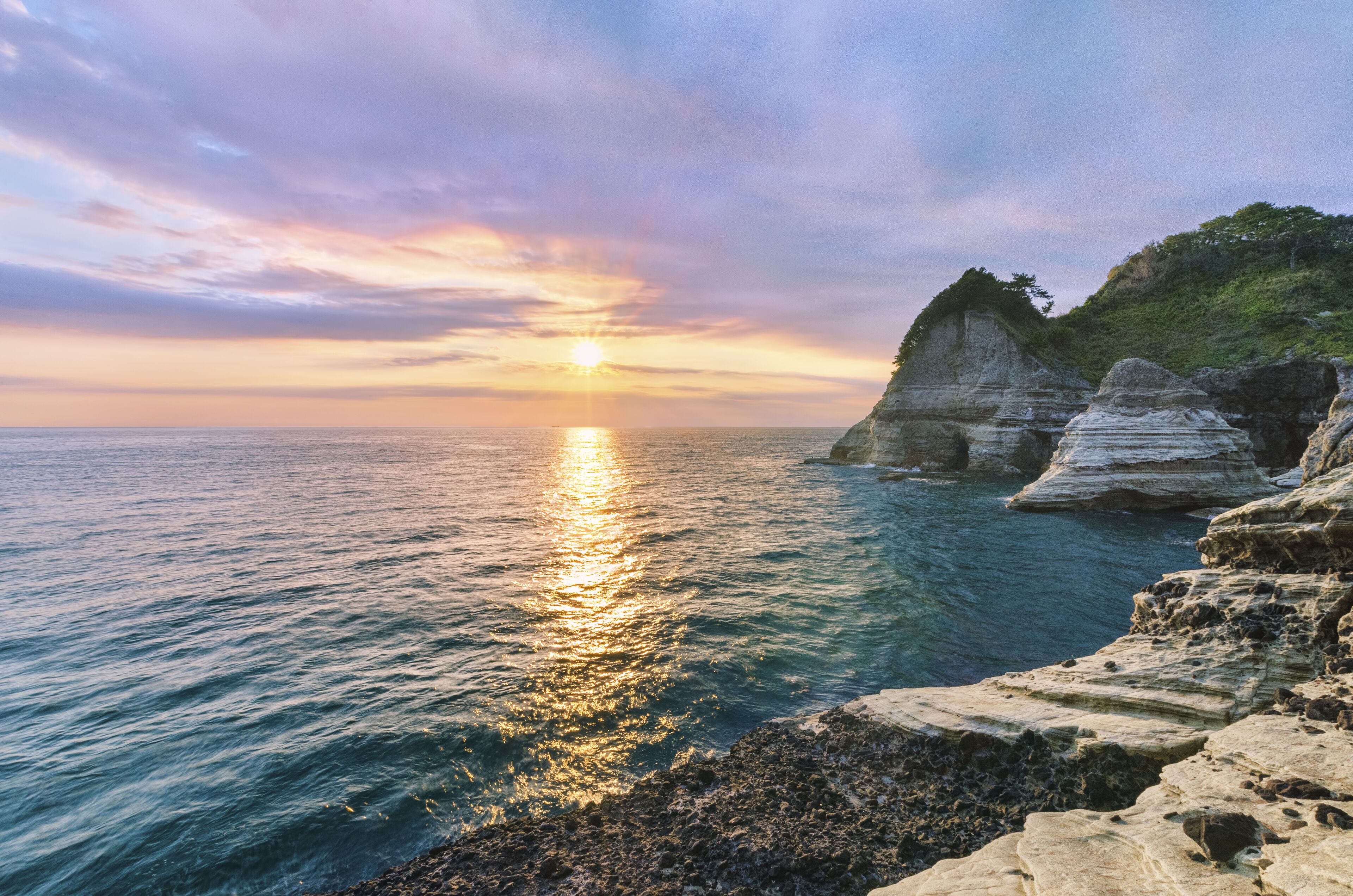 A coastal sunset with clear skies, rocky cliffs, and calm sea.