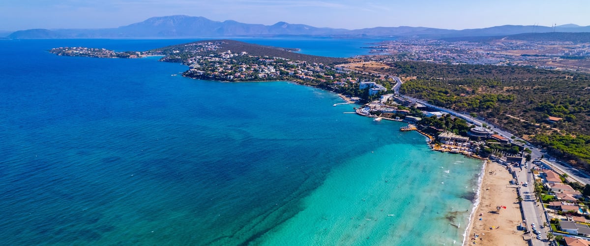 Vista aérea de un pueblo costero con playa, aguas turquesas cristalinas y un telón de fondo montañoso.