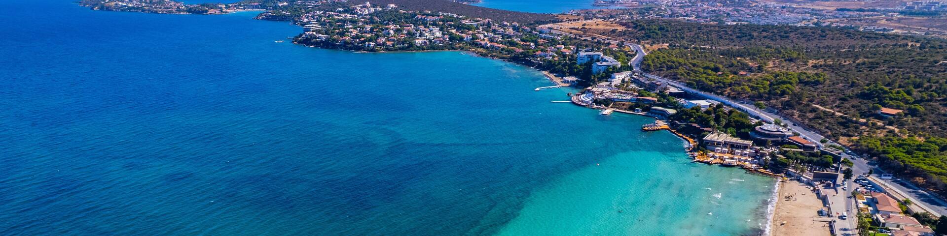 An aerial view of a coastal town with a beach, clear turquoise waters, and a mountainous backdrop.
