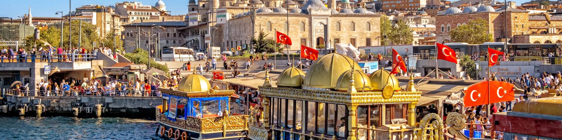 A historic mosque with two minarets, a bustling waterfront with traditional boats, and a clear blue sky.