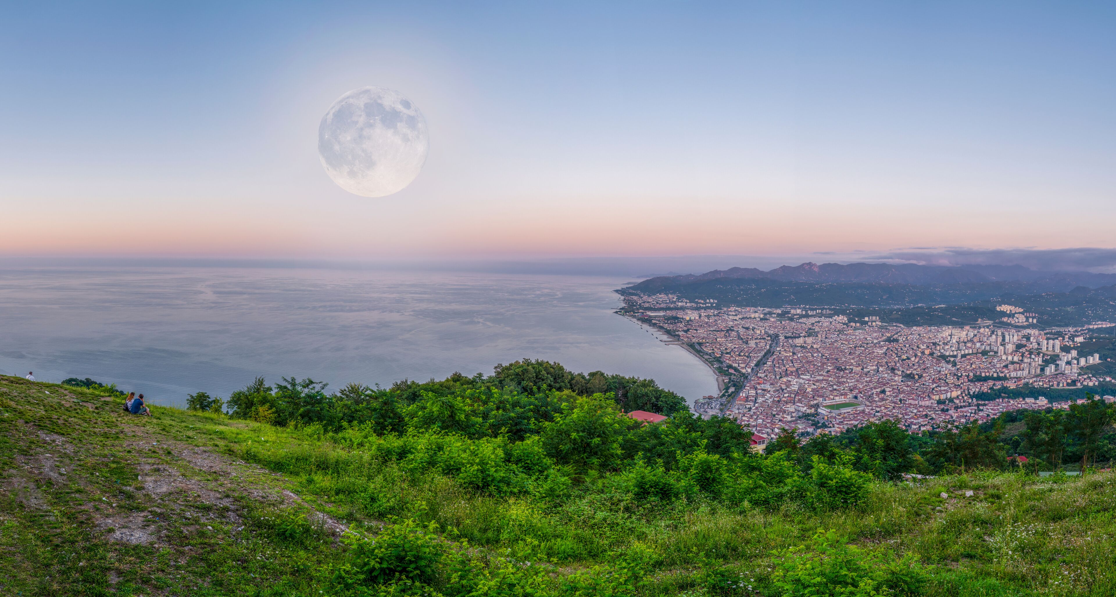 A coastal city with a large moon in the sky.