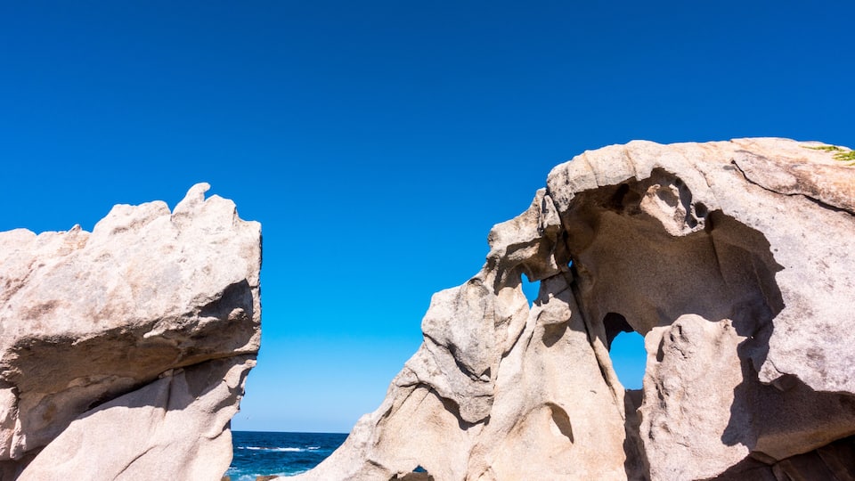 A rock formation with a natural archway and the ocean in the background.