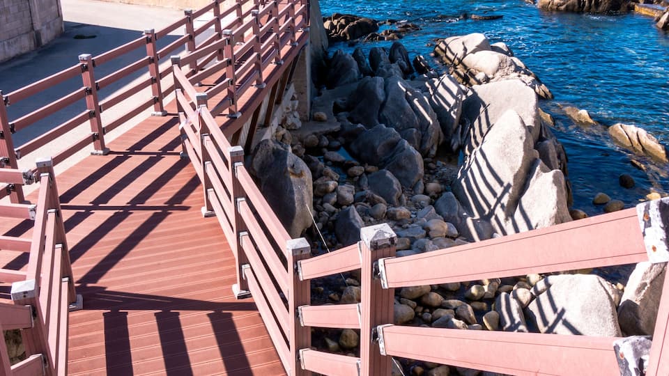 A wooden boardwalk leading to rocky cliffs by the sea.