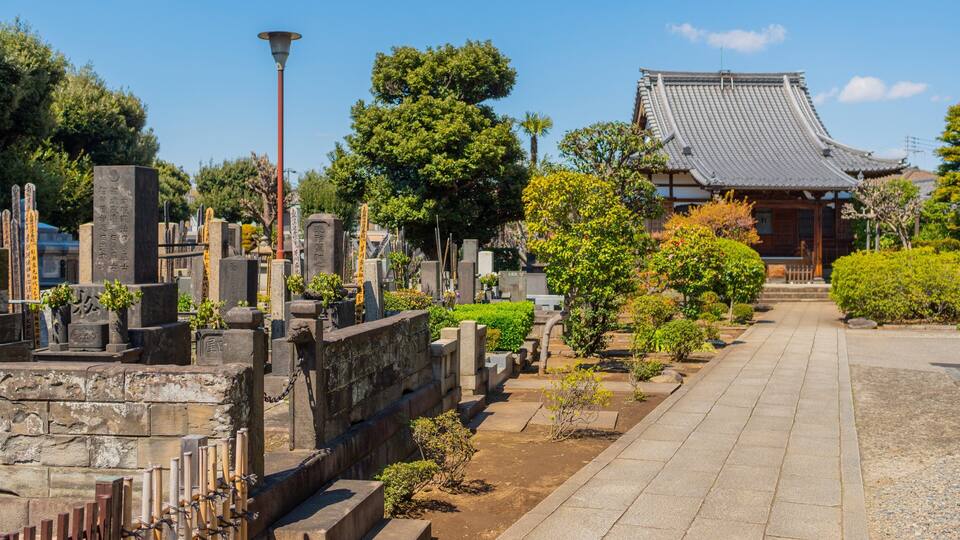 Ein traditioneller japanischer Friedhof mit Steinmalsteinen und einem Tempel im Hintergrund.