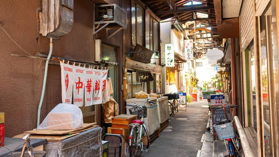 Ein schmaler Gang mit traditionellen japanischen Schildern, Fahrrädern und verschiedenen Waren, die vor Geschäften ausgestellt sind.