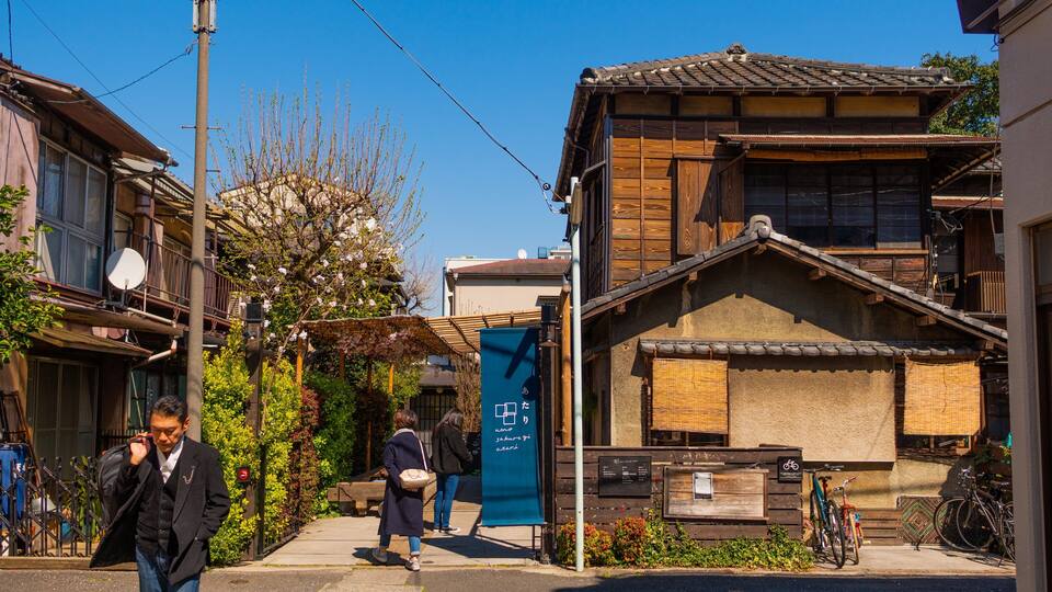 Eine traditionelle japanische Straße mit Holzhäusern, blauem Himmel und einer Person, die gerade geht.