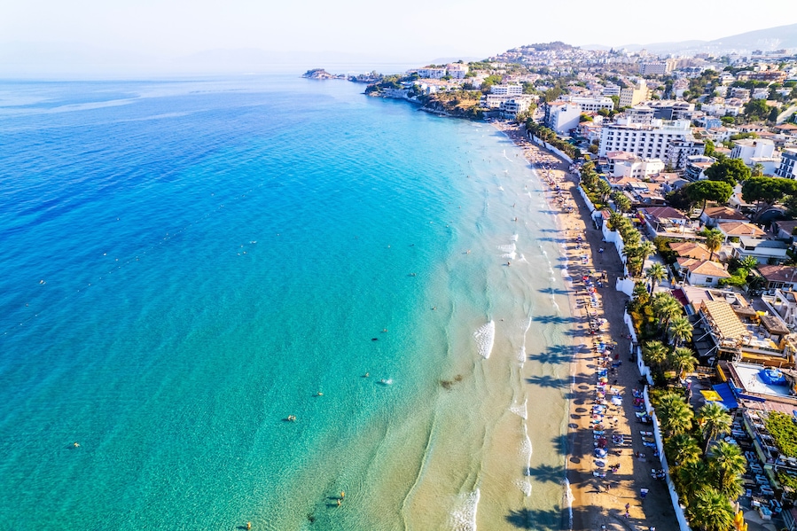 A coastal town with a clear blue sea, sandy beach, and buildings along the shore.