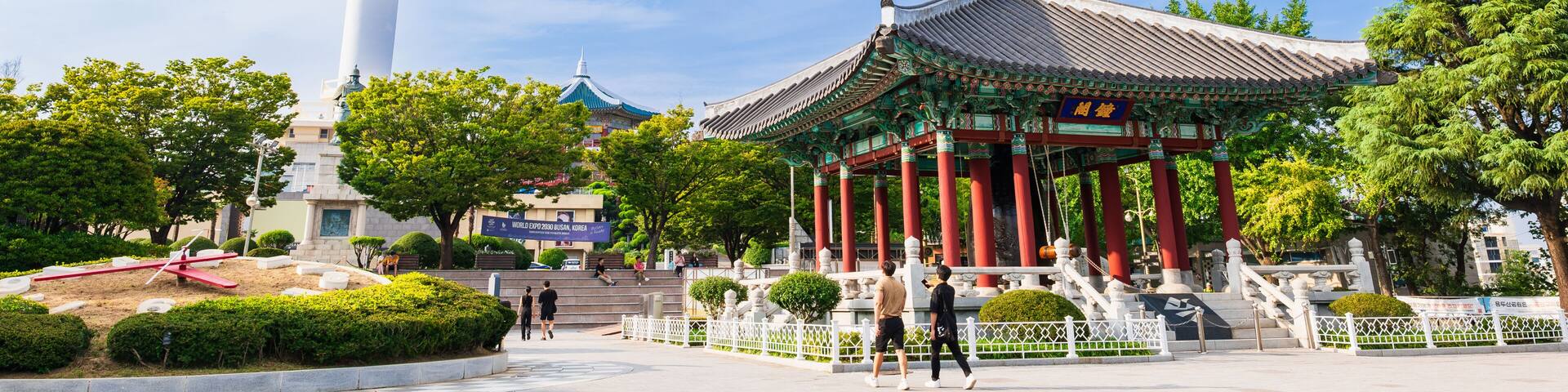 A traditional pavilion with red pillars and a white tower in the background.