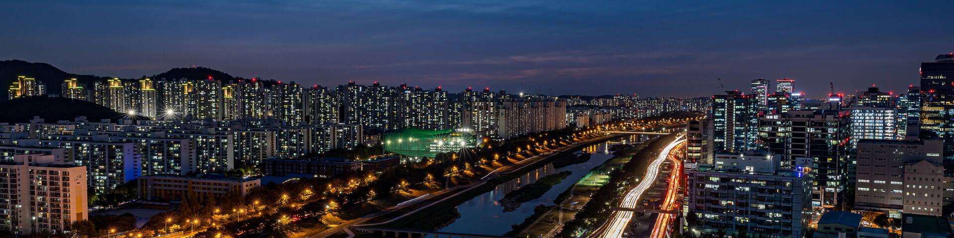 A cityscape at dusk with illuminated buildings and a river running through the center.