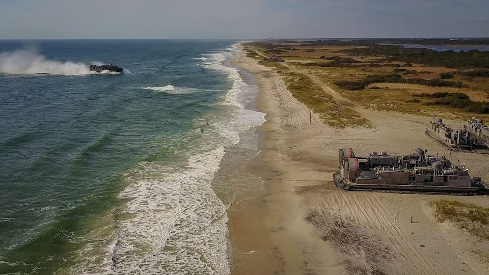 A coastal landscape with a beach, ocean waves, and a large industrial ship.