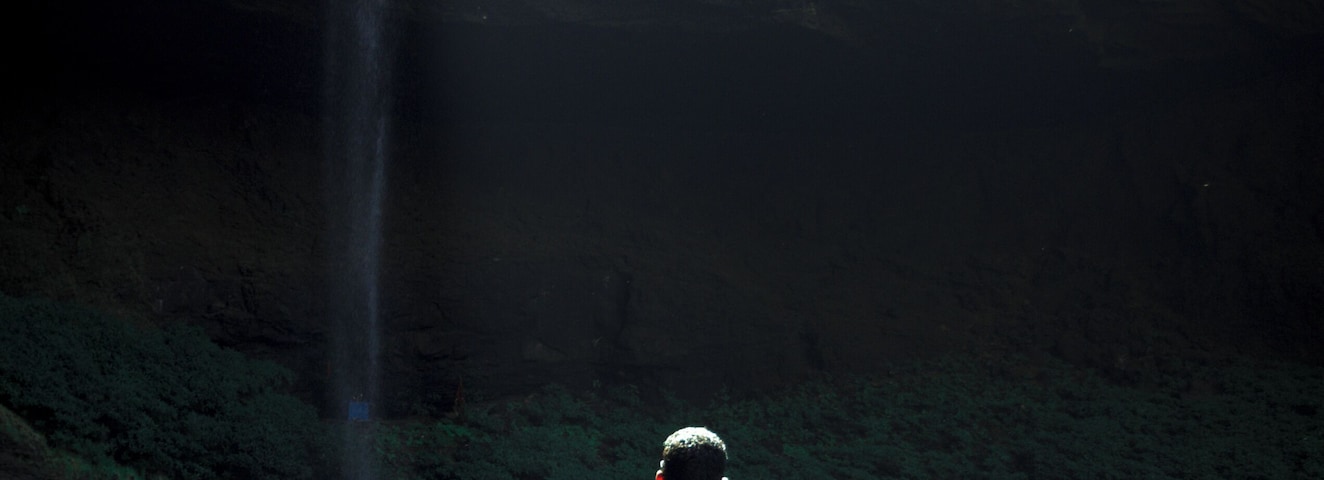 Un hombre de pie sobre una roca cerca de una cascada dentro de una cueva.