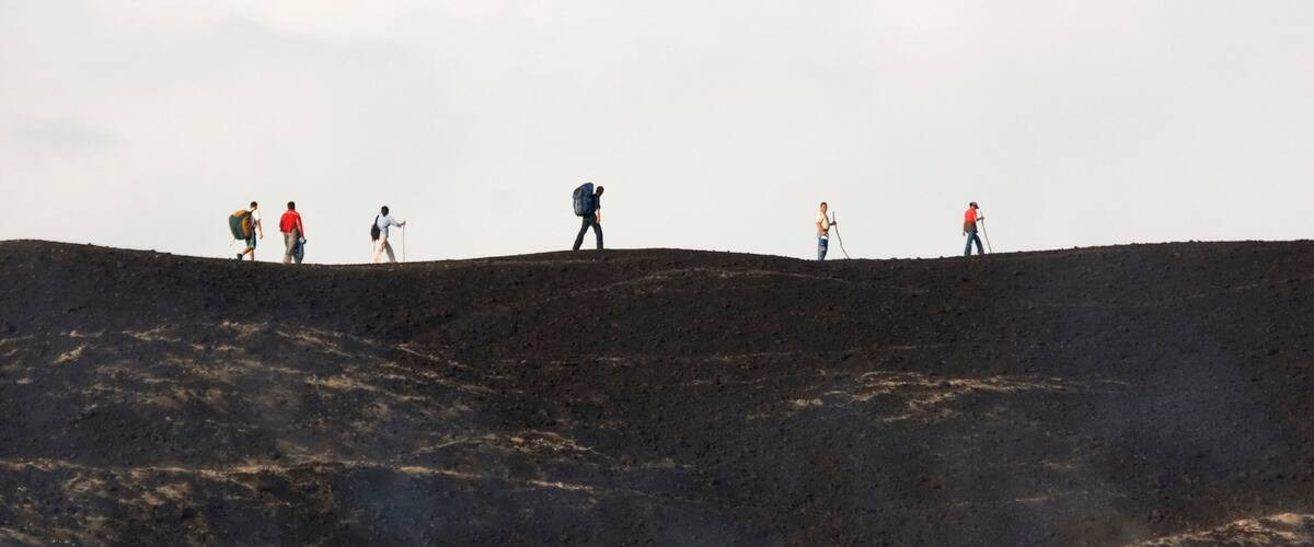 A group of hikers on a rocky, uneven terrain under a cloudy sky.