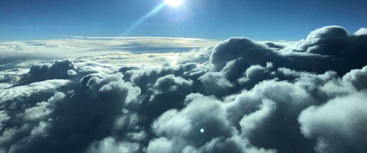 A sun shining through clouds with a moon visible in the sky.