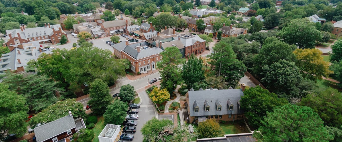 An aerial view of a town with historic buildings, a parking lot, and surrounding greenery.
