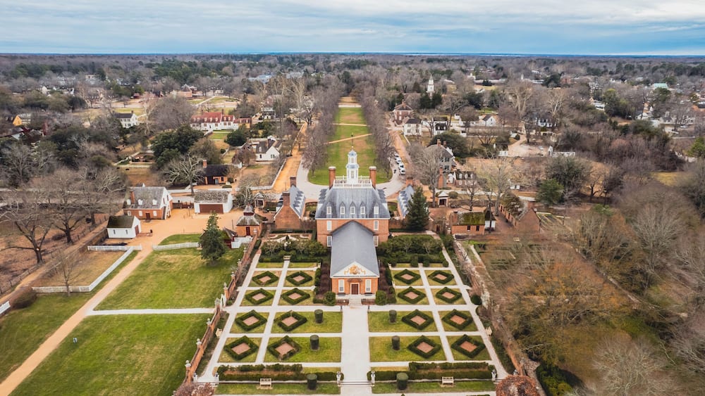 An aerial view of a historic estate with a symmetrical garden, a central building with a tower, and surrounding residential areas.
