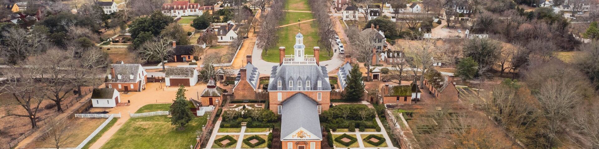 An aerial view of a historic estate with a symmetrical garden, a central building with a tower, and surrounding residential areas.